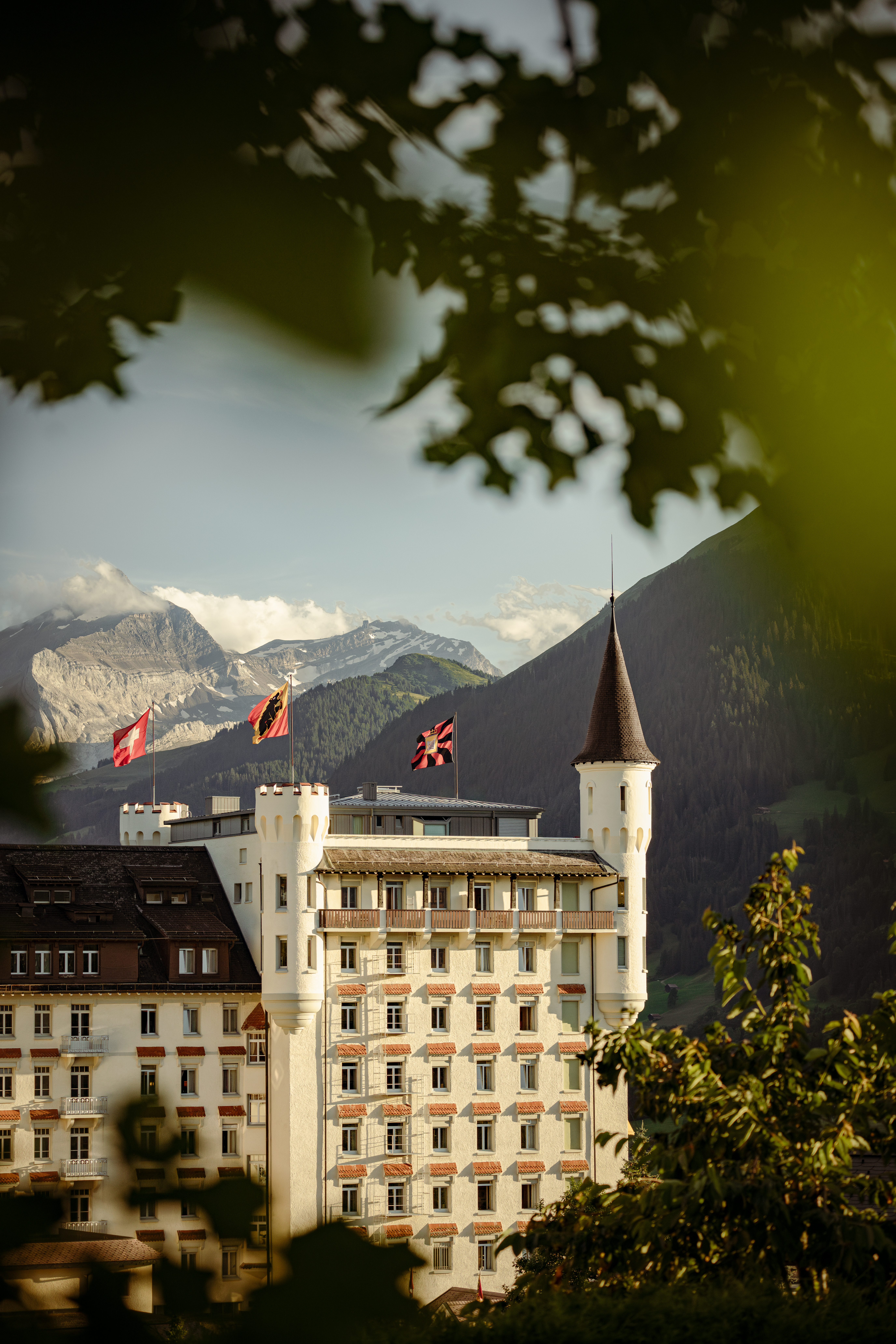 The Gstaad Palace framed by trees, with flags flying and mountains behind